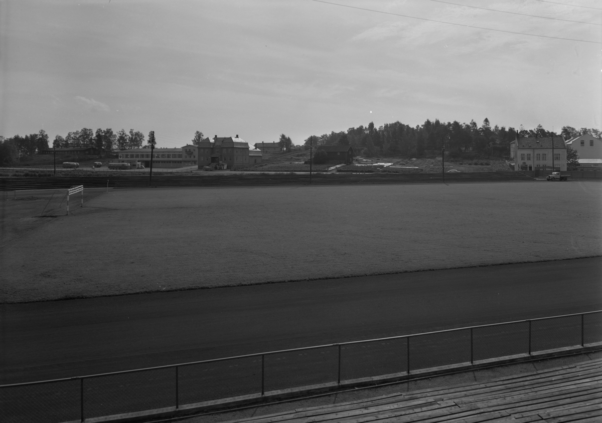 Hamar, Holset, oversiktsbilde av Hamar Stadion mot Vangsvegen. Tribuner, gressmatte, løpebane rundt gressbanen, bebyggelse i bakgrunnen med garasjeanlegget til HOB Hamar og Omland bilruter, Biografen Kino, Fuglseths gartneri,