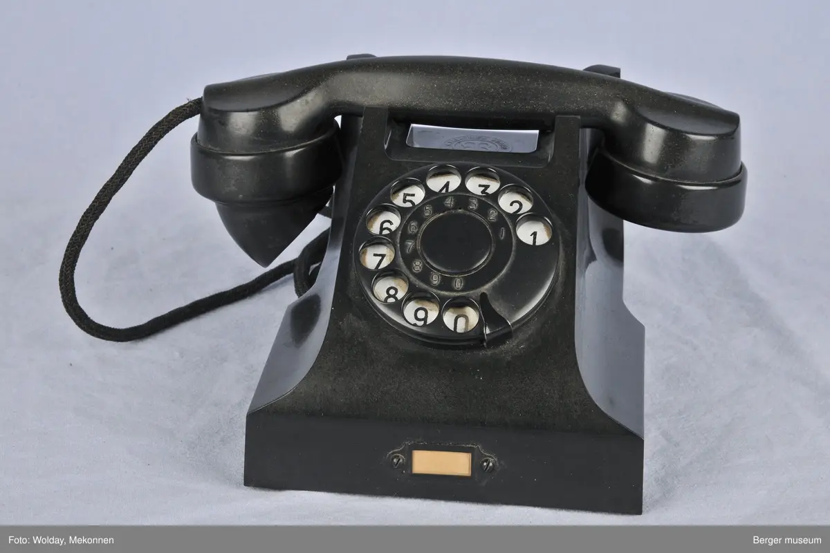 Bordtelefon. Mangler støpsel. Det er plass til å skrive nummeret på telefonen i en liten rute foran på telefonen. Normal skive.