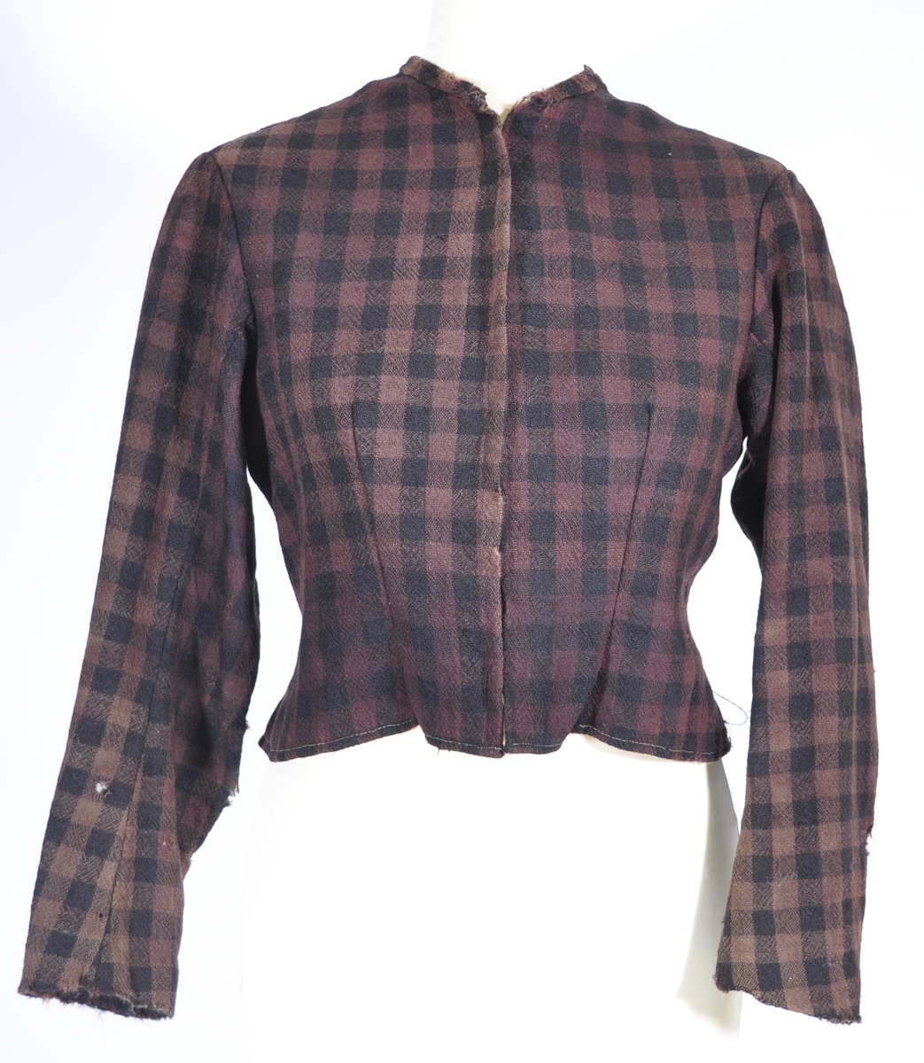 Kjoleliv i svart og brunrutet ull i hjemmevevd toskaft med ermer og bol i samme stoff. Livet er i dag velbrukt, falmet og slitt, med hull på albuene. Sydd for maskin og hånd med panelsøm og bakovertrekte skuldersømmer og sidesømmer. Rund rigning i halsen og buet fremkant. 1,5 cm bred halslinning sydd med maskin og lagt over og festet med faldesting og prikkesting i svart bomullstråd. Tett lukket med 13 par metallhekter med en 1,5 cm bred stolpe som skjuler hektingen. Kantene fremme er først sydd med maskin med brun sytråd og med leggsøm med brun bomullstråd. Livet har et innsnitt som er 3 cm på det bredeste under bysten, sydd med maskin. Smal tosøms krokarm. Livet er helfôret med ubleket bomull i hjemmevevd toskaft og sydd på samtidig som ullstoffet ble sydd sammen med maskin og spilesøm med tykk bomullstråd for hånd. Livet brukes ned i stakken og har hatt en metallkrok midt på bak til å hekte stakken på.