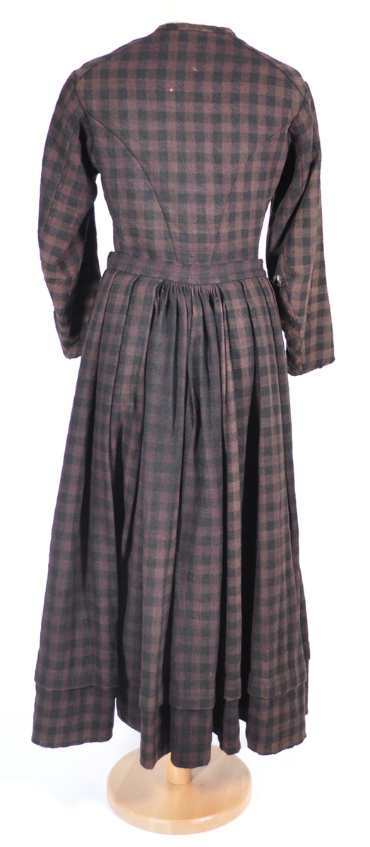 Kjoleliv i svart og brunrutet ull i hjemmevevd toskaft med ermer og bol i samme stoff. Livet er i dag velbrukt, falmet og slitt, med hull på albuene. Sydd for maskin og hånd med panelsøm og bakovertrekte skuldersømmer og sidesømmer. Rund rigning i halsen og buet fremkant. 1,5 cm bred halslinning sydd med maskin og lagt over og festet med faldesting og prikkesting i svart bomullstråd. Tett lukket med 13 par metallhekter med en 1,5 cm bred stolpe som skjuler hektingen. Kantene fremme er først sydd med maskin med brun sytråd og med leggsøm med brun bomullstråd. Livet har et innsnitt som er 3 cm på det bredeste under bysten, sydd med maskin. Smal tosøms krokarm. Livet er helfôret med ubleket bomull i hjemmevevd toskaft og sydd på samtidig som ullstoffet ble sydd sammen med maskin og spilesøm med tykk bomullstråd for hånd. Livet brukes ned i stakken og har hatt en metallkrok midt på bak til å hekte stakken på.