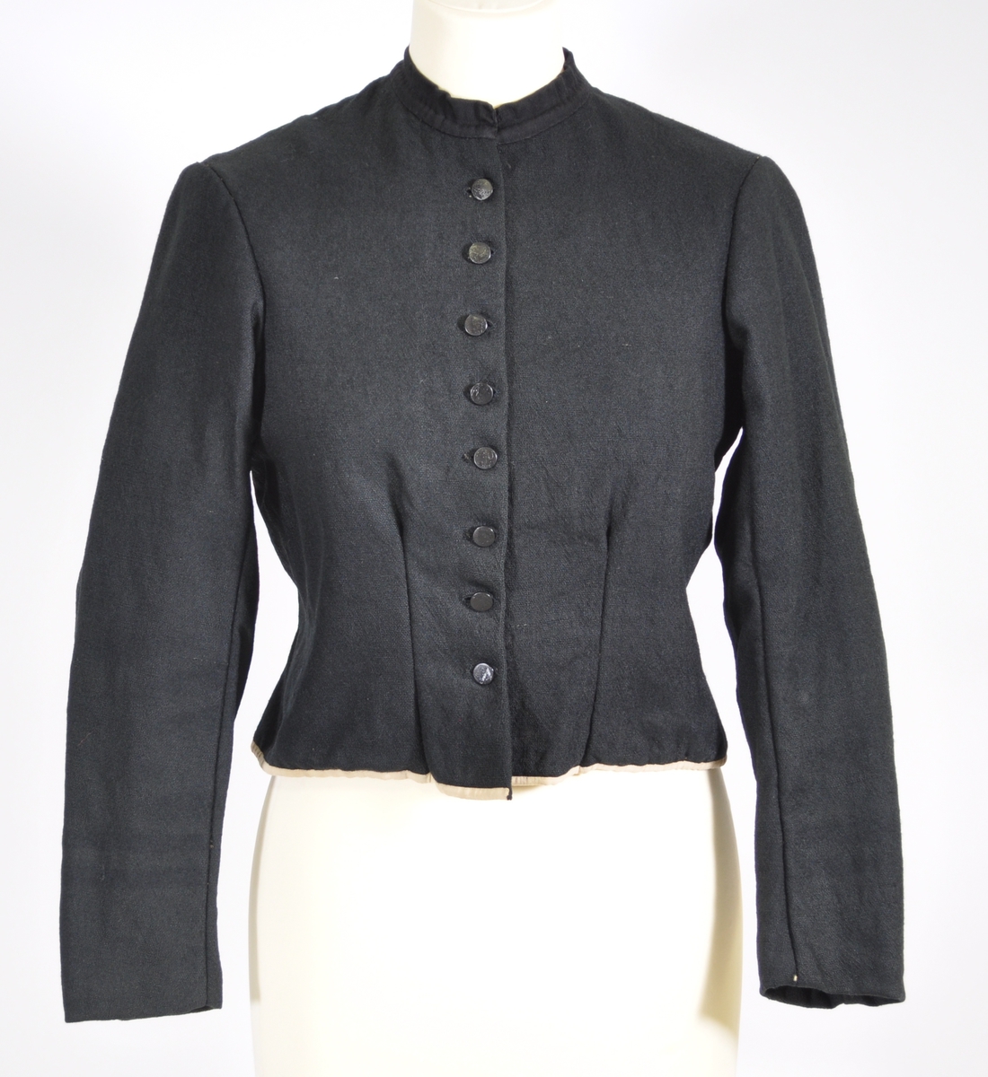 Kjoleliv i svart ull i hjemmevevd toskaft med ermer og bol i samme stoff. Livet er i dag i god stand med noen hull og ellers liten slitasje. Sydd for maskin og hånd med panelsøm og bakovertrekte skuldersømmer og sidesømmer. Rund rigning i halsen og buet fremkant. 2,5 cm bred halslinning i svart kjøpebånd i bomull, sydd på med faldesting og prikkesting med svart bomullstråd. Lukket med 8 svarte kjøpeknapper med preget blomstermønster i horn. Knapphullene er sydd for hånd med svart ulltråd og brun lintråd. Livet har et innsnitt som er 3 cm på det bredeste under bysten, sydd med maskin. Smal tosøms krokarm. Livet er helfôret med ubleket og grå bomull i fiskebensmønster i hjemmevevd toskaft og sydd på samtidig som ullstoffet ble sydd sammen med maskin og spilesøm med tykk bomullstråd for hånd. Nedkanten av livet er kantet med et 0,5 cm bredt ubleket bomullsbånd i hjemmevevd toskaft, sydd på med maskin, lagt over og festet med faldesting for hånd med brun bomullstråd. Midt på bak har livet en 5 cm lang splitt, også kantet med bomullsbåndet. Livet brukes ned i stakken og har en påsydd metallkrok bak til å hekte stakken på.