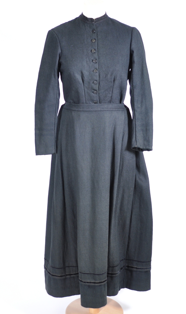 Kjoleliv i svart ull i hjemmevevd toskaft med ermer og bol i samme stoff. Livet er i dag i god stand med noen hull og ellers liten slitasje. Sydd for maskin og hånd med panelsøm og bakovertrekte skuldersømmer og sidesømmer. Rund rigning i halsen og buet fremkant. 2,5 cm bred halslinning i svart kjøpebånd i bomull, sydd på med faldesting og prikkesting med svart bomullstråd. Lukket med 8 svarte kjøpeknapper med preget blomstermønster i horn. Knapphullene er sydd for hånd med svart ulltråd og brun lintråd. Livet har et innsnitt som er 3 cm på det bredeste under bysten, sydd med maskin. Smal tosøms krokarm. Livet er helfôret med ubleket og grå bomull i fiskebensmønster i hjemmevevd toskaft og sydd på samtidig som ullstoffet ble sydd sammen med maskin og spilesøm med tykk bomullstråd for hånd. Nedkanten av livet er kantet med et 0,5 cm bredt ubleket bomullsbånd i hjemmevevd toskaft, sydd på med maskin, lagt over og festet med faldesting for hånd med brun bomullstråd. Midt på bak har livet en 5 cm lang splitt, også kantet med bomullsbåndet. Livet brukes ned i stakken og har en påsydd metallkrok bak til å hekte stakken på.