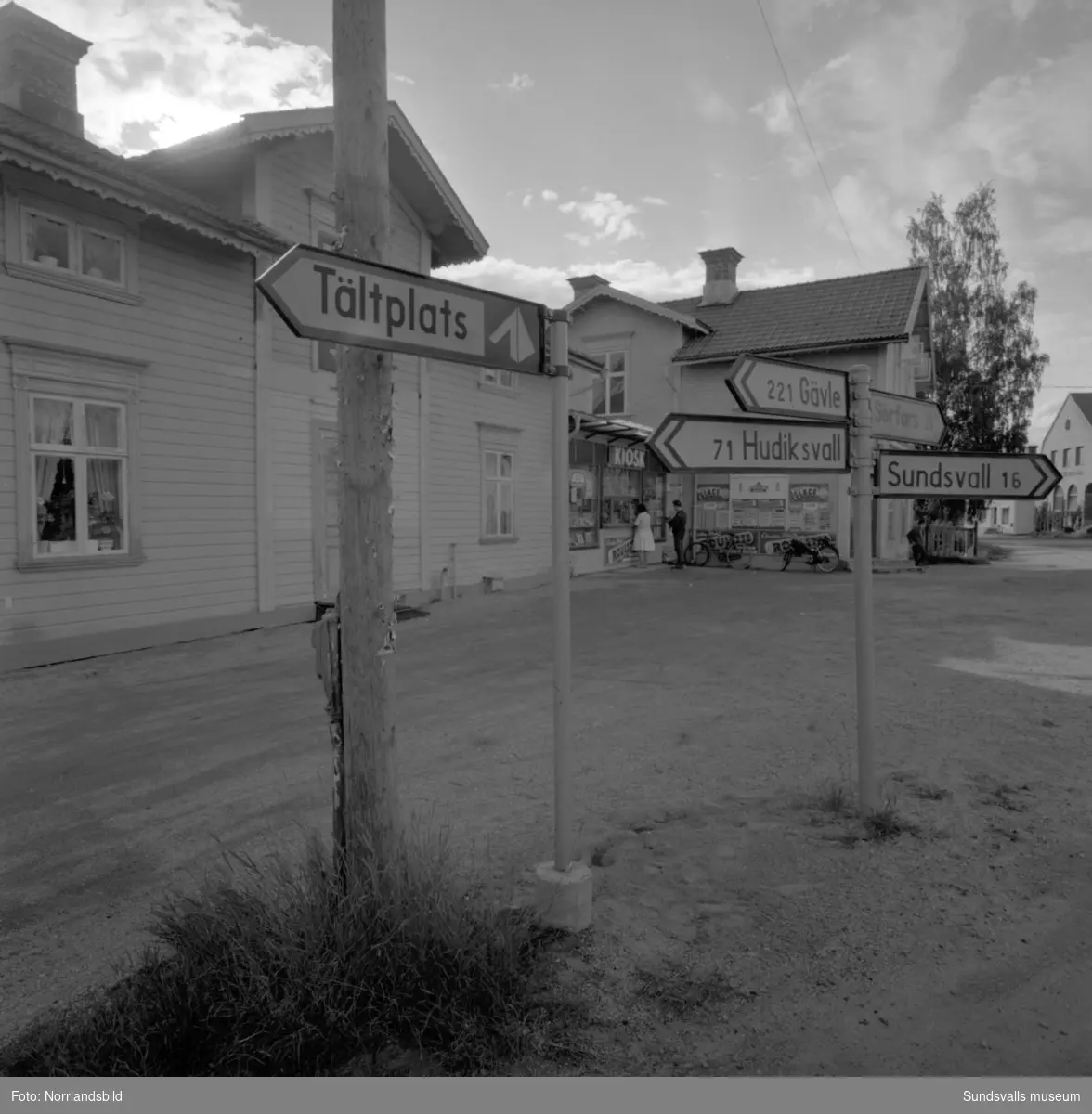 Skyltning utefter vägen mellan Sundsvall och hälsingegränsen 1961. Bland annat Bergafjärden, Dingersjö, Bredsand och Kusten. I Njurundabommen fick länge trafikanterna söderifrån lätta på gasen och anamma ett makligare tempo. Men innan vägen som nu blivit ”gamla E4:an” byggdes, var det så här som korsningen i Bommen såg ut. Längst till höger i bild skymtar det före detta bankhuset som fortfarande finns kvar.