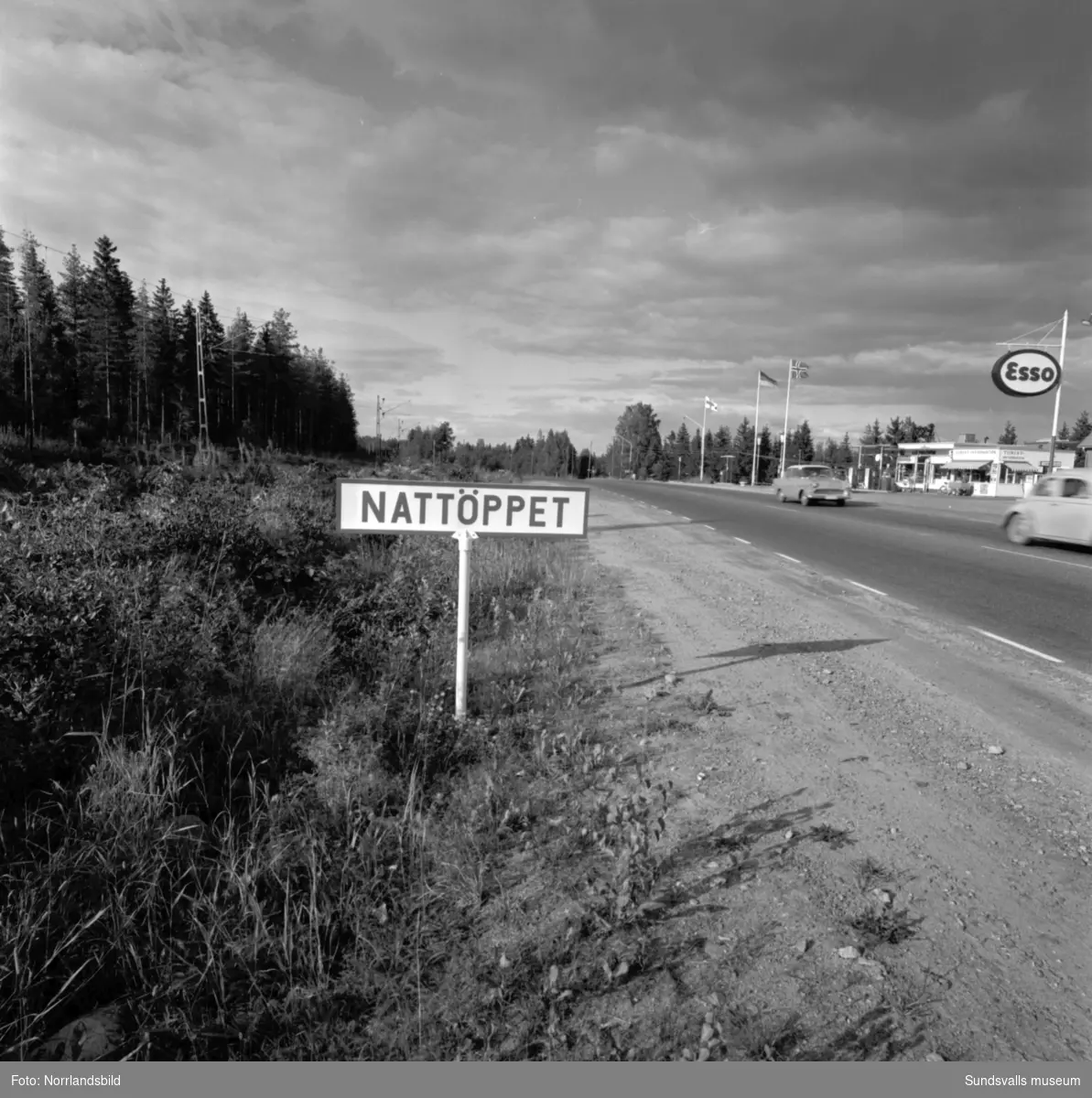 Skyltning utefter vägen mellan Sundsvall och hälsingegränsen 1961. Bland annat Bergafjärden, Dingersjö, Bredsand och Kusten. I Njurundabommen fick länge trafikanterna söderifrån lätta på gasen och anamma ett makligare tempo. Men innan vägen som nu blivit ”gamla E4:an” byggdes, var det så här som korsningen i Bommen såg ut. Längst till höger i bild skymtar det före detta bankhuset som fortfarande finns kvar.