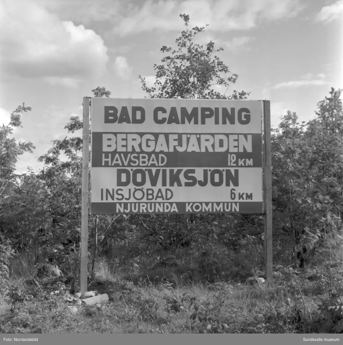 Skyltning utefter vägen mellan Sundsvall och hälsingegränsen 1961. Bland annat Bergafjärden, Dingersjö, Bredsand och Kusten. I Njurundabommen fick länge trafikanterna söderifrån lätta på gasen och anamma ett makligare tempo. Men innan vägen som nu blivit ”gamla E4:an” byggdes, var det så här som korsningen i Bommen såg ut. Längst till höger i bild skymtar det före detta bankhuset som fortfarande finns kvar.