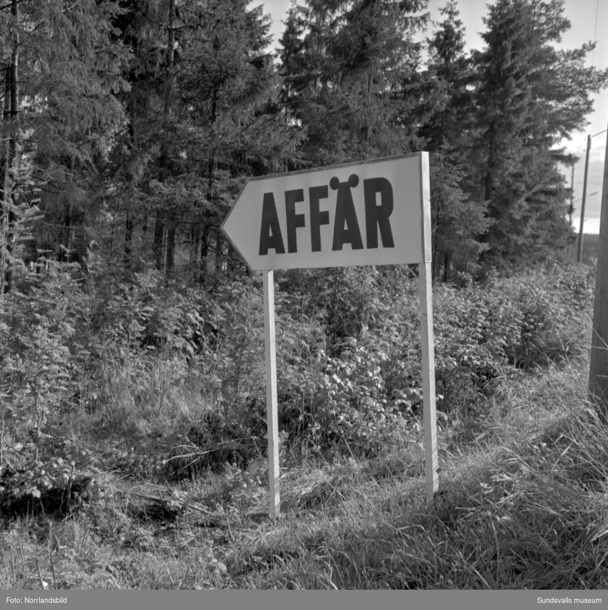 Skyltning utefter vägen mellan Sundsvall och hälsingegränsen 1961. Bland annat Bergafjärden, Dingersjö, Bredsand och Kusten. I Njurundabommen fick länge trafikanterna söderifrån lätta på gasen och anamma ett makligare tempo. Men innan vägen som nu blivit ”gamla E4:an” byggdes, var det så här som korsningen i Bommen såg ut. Längst till höger i bild skymtar det före detta bankhuset som fortfarande finns kvar.