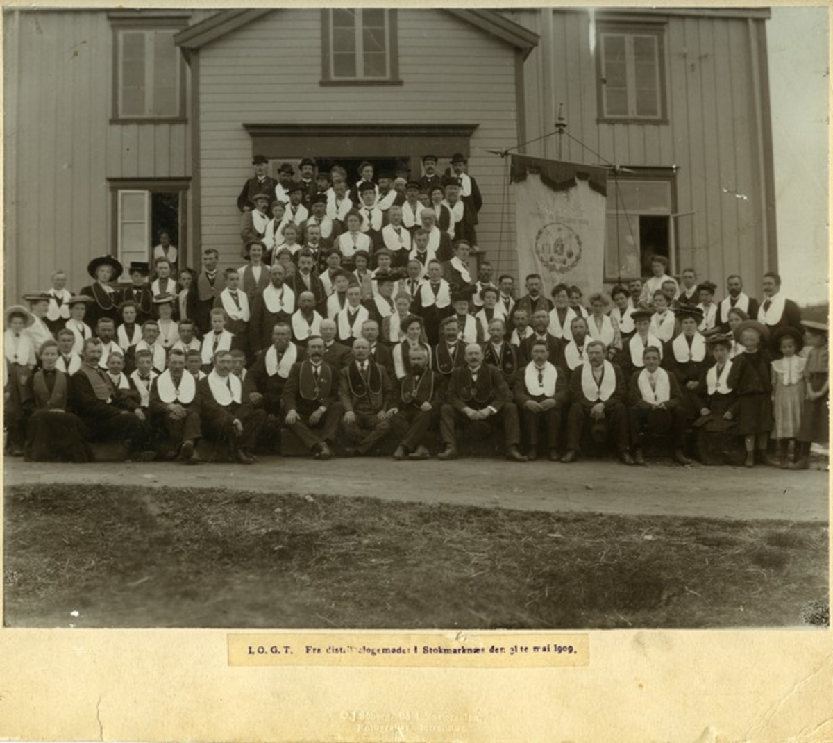 Avholdmøte, Stokmarknes, Hadsel. Notert under bildet. "I.O.G.T. Fra distriktslogemødet i Stokmarknæs den 31ste mai 1909". Fanen har tekst "IOGT. Loge Narvik".