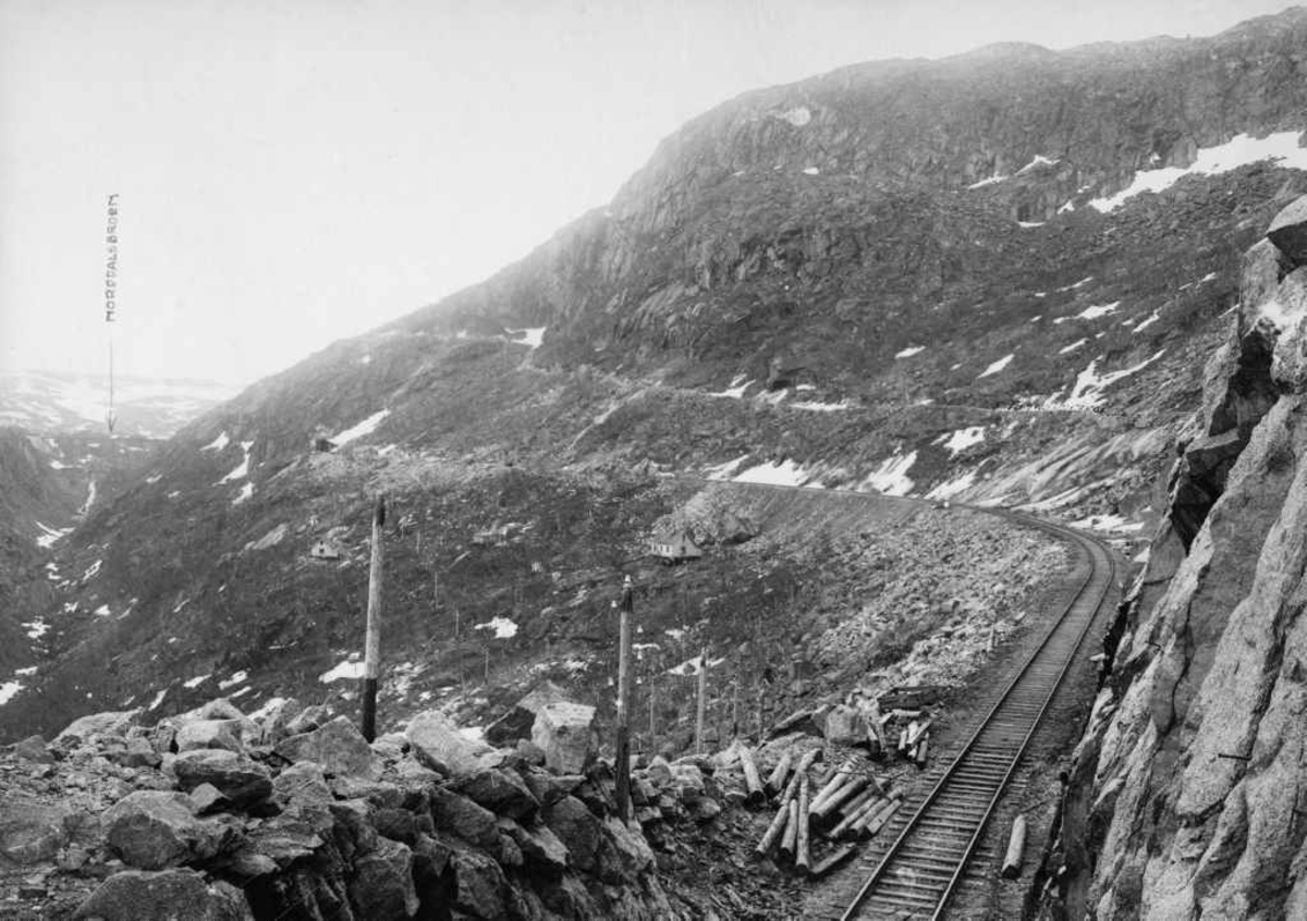 Ofotbanen. Jernbanetrasee og anleggsvei/ rallarvei. Norddalen. Norddalsbrua til v. Vestre åpning til Norddalsbrutunnelen til h. for brua.
Ofotbanens anleggsvei