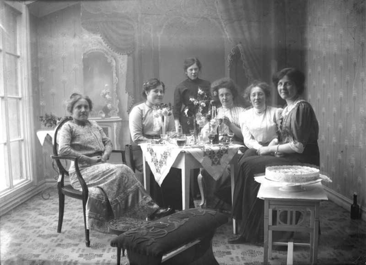 Seks damer drikker vin rundt et bord. Til høyre Magdalene og Claudia. Bildet er fra atelieret i Harstad. Til venstre sitter Anna Hansen (Kulseng).