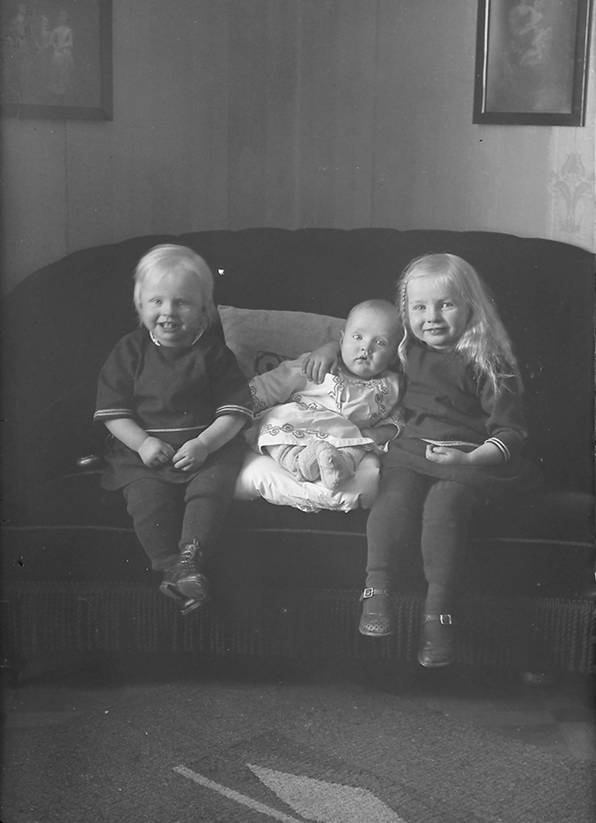 Portrett. 3 unger sitter i en sofa, ca. 1 - 4 år.Bildet er tatt på Reine i Lofoten.  Interiør