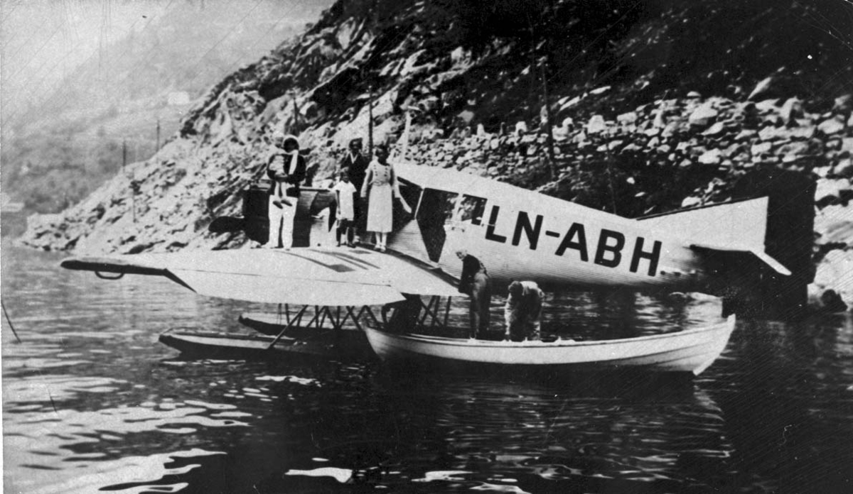 1 fly på havet, Junkers Ju34 LN-ABH fra Norges Aero A/S, Narvik. 1 åpen båt (tilbringerbåt) ved flyey. Flere personer i båten og på ene fly vingen.