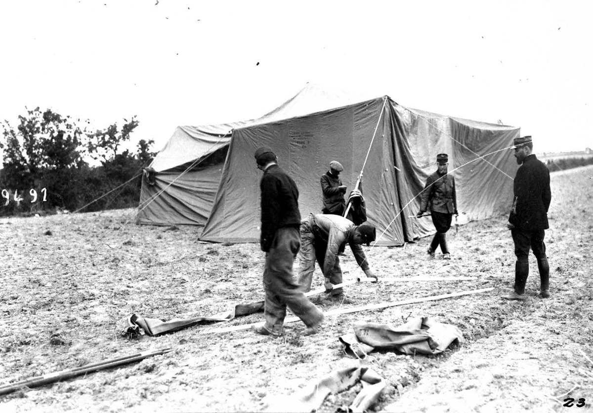 Ett telt (skvadrontelt) for militært personell. Flere personer, menn i militæruniform, i forgrunnen.