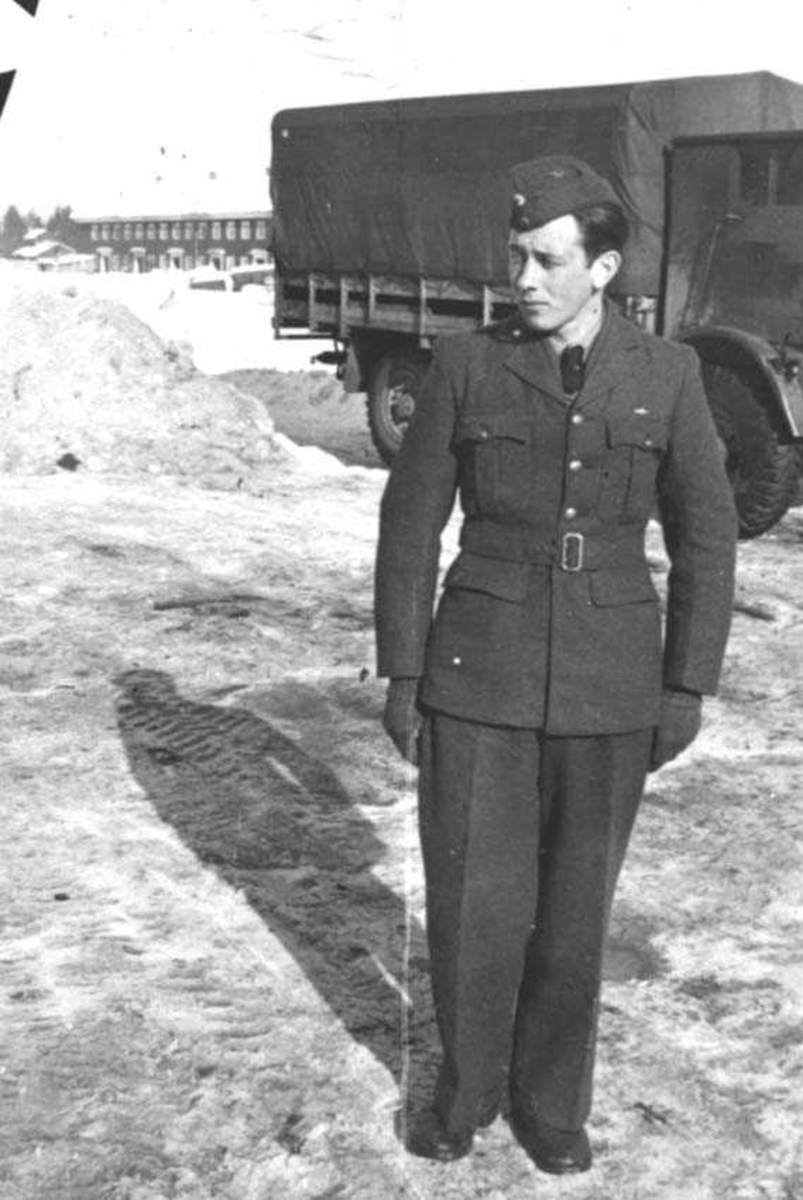 En person i militæruniform. Mann. Lastebil og bygning i bakgrunnen.