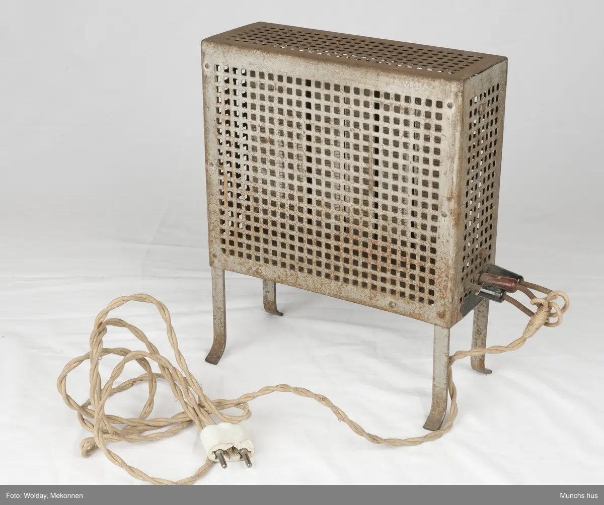 Elektrisk varmeovn. Ovnen yter 1000 Watt - 220 Volt. 
Merket Volta.
Laget av forniklet eller galvanisert jern som er utstyrt med firkantete huller, ca. 1320 stk. den flettede lednikngen er koblet til ovnen med tre plugger, to sorte og en rød. Lednikngen er ca. 290 cm lang og utstyrt med et stort støpsel i porselen. Ovnen har ingen bryter.