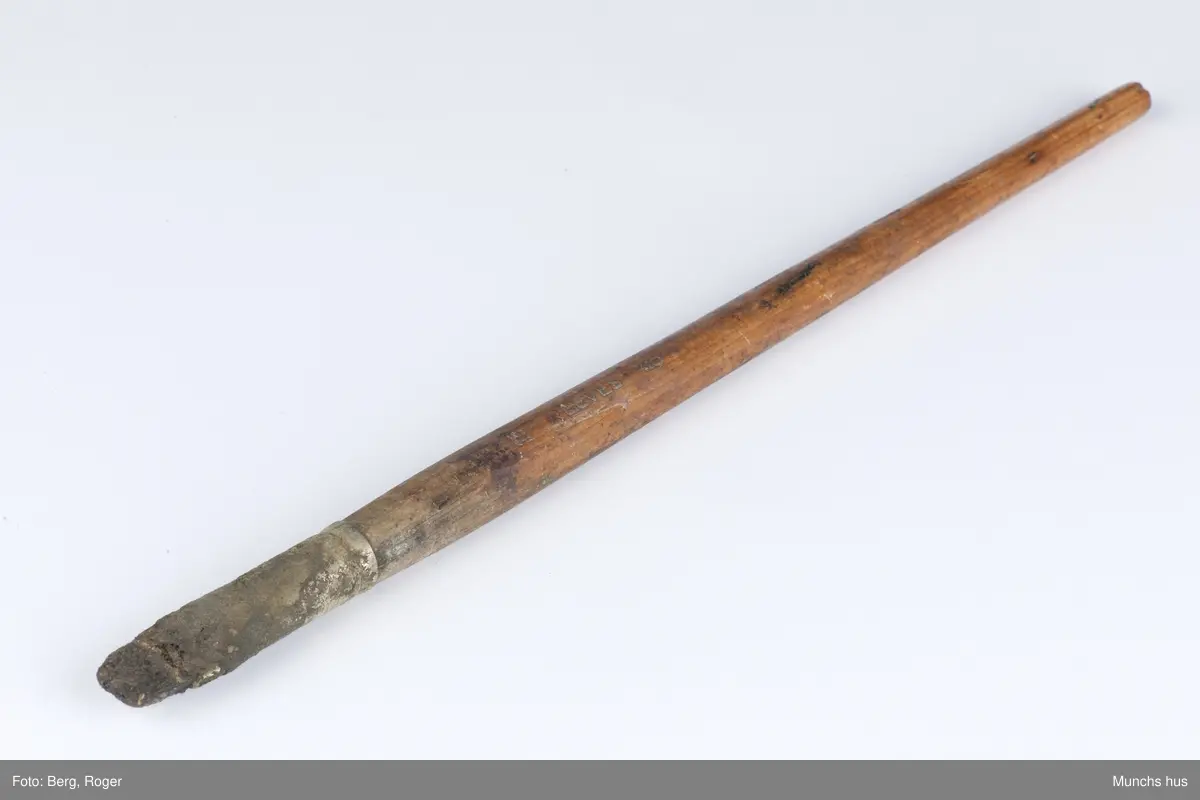 Flat malepensel med treskaft. Busten er stiv. Beslaget er blankt, men sterkt anløpet.