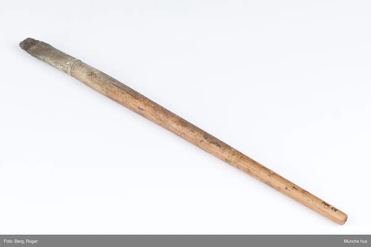 Flat malepensel med treskaft. Busten er stiv. Beslaget er blankt, men sterkt anløpet.