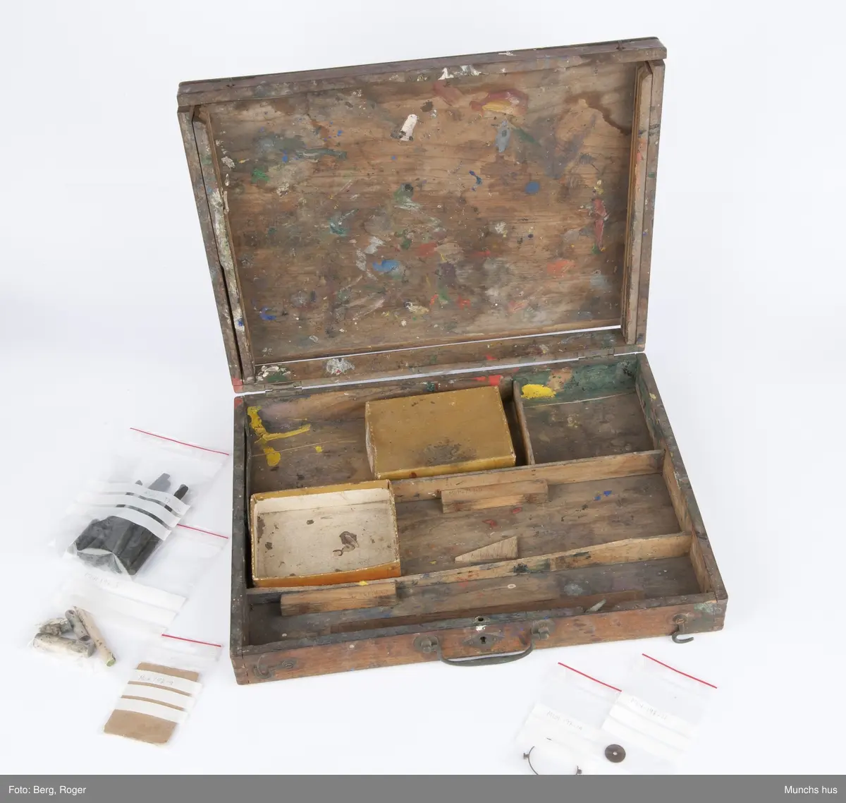 Malerskrin, hengslet i bakkant. Det er fire rom i bunn. Innhold i skrinet: 1 eske (med lokk) med påklistret lapp: CADMIUM ROUGHE BLOCKY J. Blockx Fils, Terwagne (Belgique) innholder 20 kullstiftbiter. 1 eske (mangler lokk) innholder 3 fargestifter (Grønn: TRADE MARK "CRAYOLA" BINNY & SMITH CO. NEW YORK. Brun: Faber. Grå: 169, L. F. Raffael.. Dusseldorf, samt rester av hvit farge fra en malingtube ant.
1 ti-øring fra 19(4?)9 ? 4 trebiter i ulike størrelser, en pappbit med anker som motiv, samt bokstavene L F.