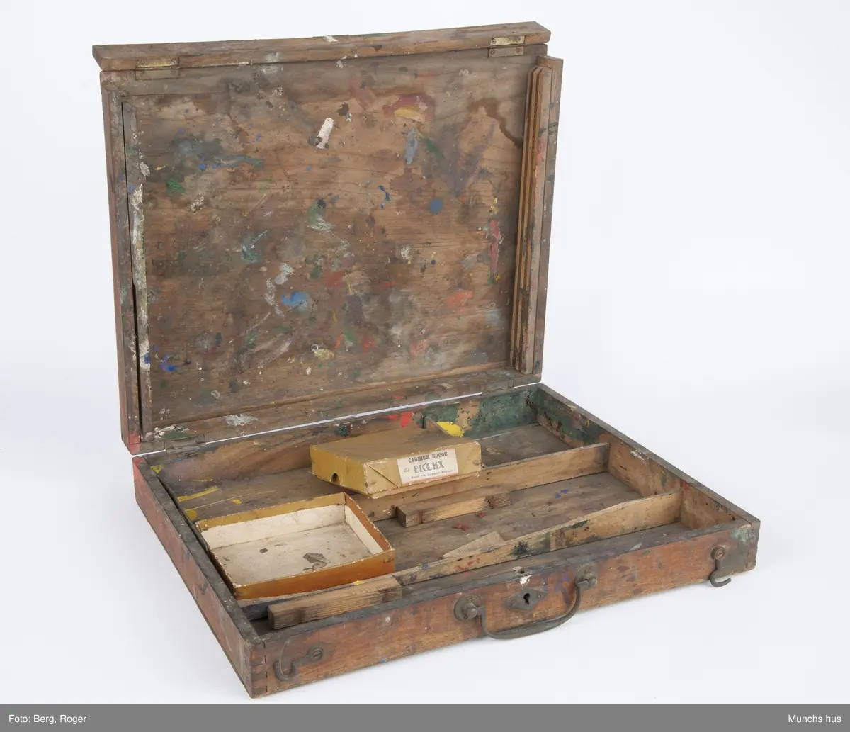 Malerskrin, hengslet i bakkant. Det er fire rom i bunn. Innhold i skrinet: 1 eske (med lokk) med påklistret lapp: CADMIUM ROUGHE BLOCKY J. Blockx Fils, Terwagne (Belgique) innholder 20 kullstiftbiter. 1 eske (mangler lokk) innholder 3 fargestifter (Grønn: TRADE MARK "CRAYOLA" BINNY & SMITH CO. NEW YORK. Brun: Faber. Grå: 169, L. F. Raffael.. Dusseldorf, samt rester av hvit farge fra en malingtube ant.
1 ti-øring fra 19(4?)9 ? 4 trebiter i ulike størrelser, en pappbit med anker som motiv, samt bokstavene L F.