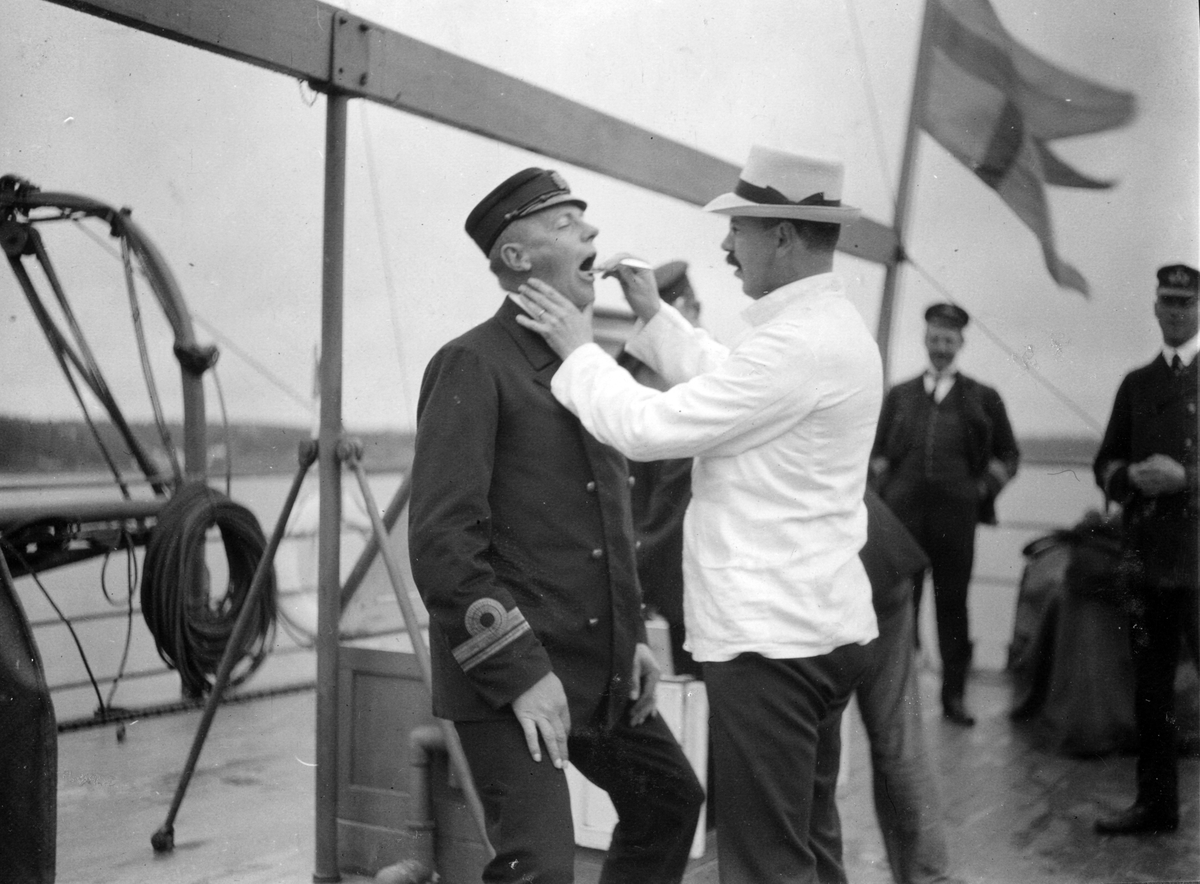 Tandläkare undersöker man uppe på däck 1911. I bakgrunden står två män och kollar på.
