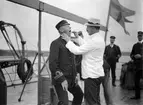 Tandläkare undersöker man uppe på däck 1911. I bakgrunden står två män och kollar på.