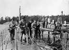 Matroser och sjöbefäl ombord på fartyget Hvalen intill brygga. En ung man står till vänster i bild med en hink i handen under ubåtskolan 1911.