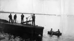 Marstrand  1916-1917. Fyra sjömän står på ubåtsdäck och kollar ner i vattnet där en jolle glider förbi med två personer i.