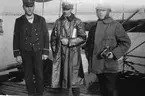 Tre män poserar framför kameran, varav en är löjtnant Netzler, aug 1917. I bakgrunden syns ett flygplan. Han störtade vid Toras Ungar i Lysekil. Avliden 15 juli 1918.