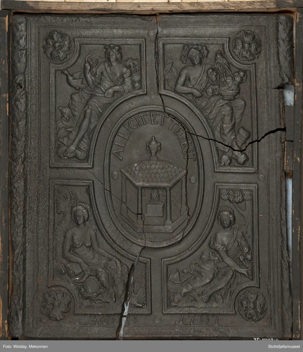 På begge sider, bladkrans. Midt på, et ovalt felt med alter og ild. Rundt feltets overkant er det en innskrift: "Allicit et terret". Rundt midtfeltet er det 4 firkantede felt med allegoriske figurer. Under er innskriften "Anno 1707".