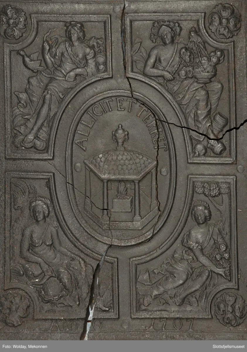 På begge sider, bladkrans. Midt på, et ovalt felt med alter og ild. Rundt feltets overkant er det en innskrift: "Allicit et terret". Rundt midtfeltet er det 4 firkantede felt med allegoriske figurer. Under er innskriften "Anno 1707".