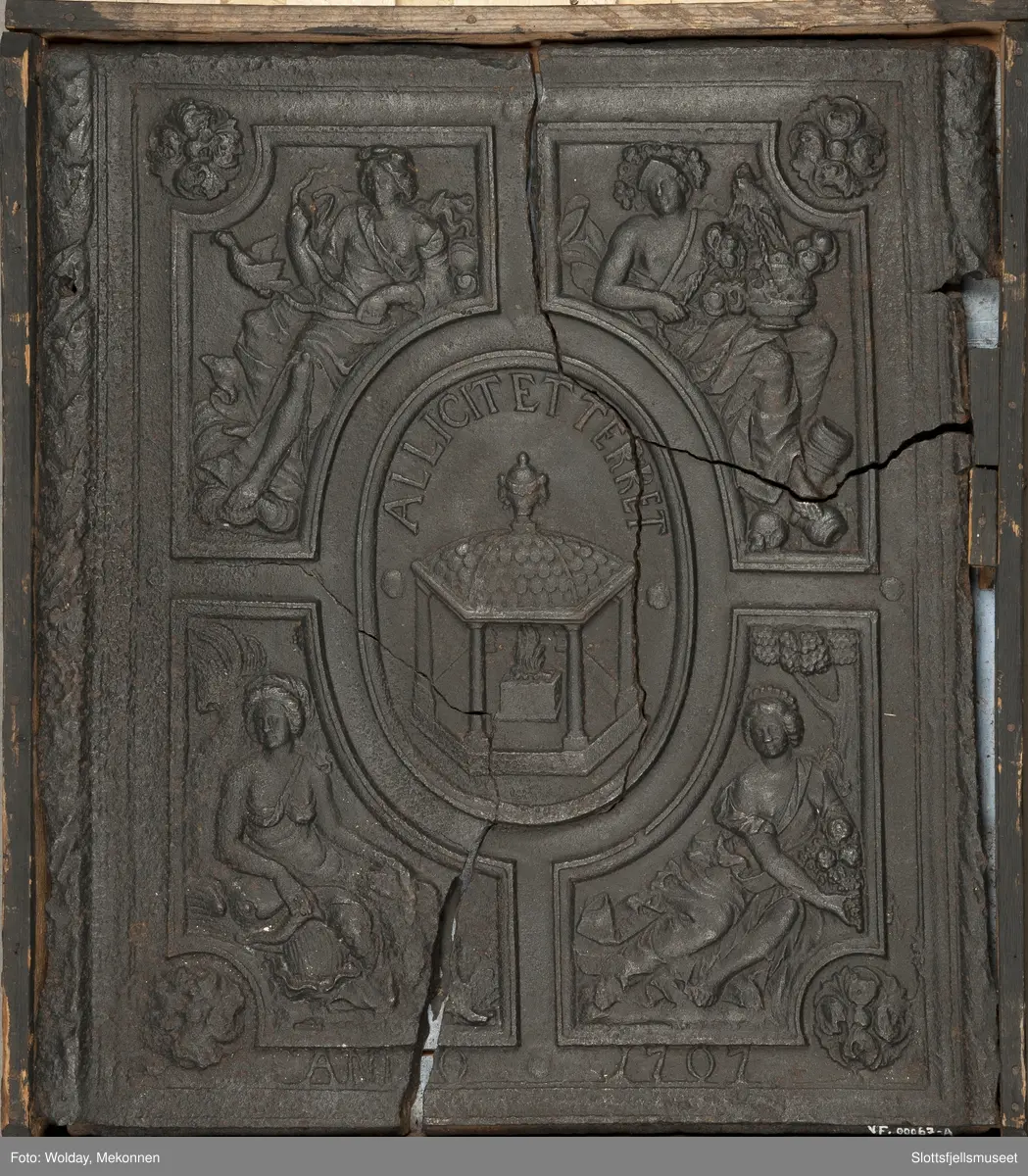 På begge sider, bladkrans. Midt på, et ovalt felt med alter og ild. Rundt feltets overkant er det en innskrift: "Allicit et terret". Rundt midtfeltet er det 4 firkantede felt med allegoriske figurer. Under er innskriften "Anno 1707".