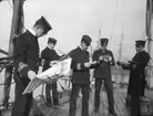 En grupp officerare läser post och tidningar på däck.