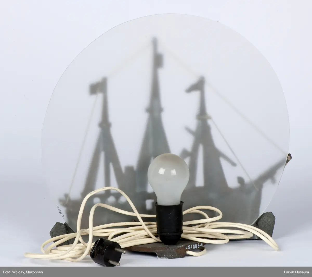 Støpt relieff av FRAM montert som lampe med børstet glass-bakgrunn, satt på hylle. Med ledning og kontakt