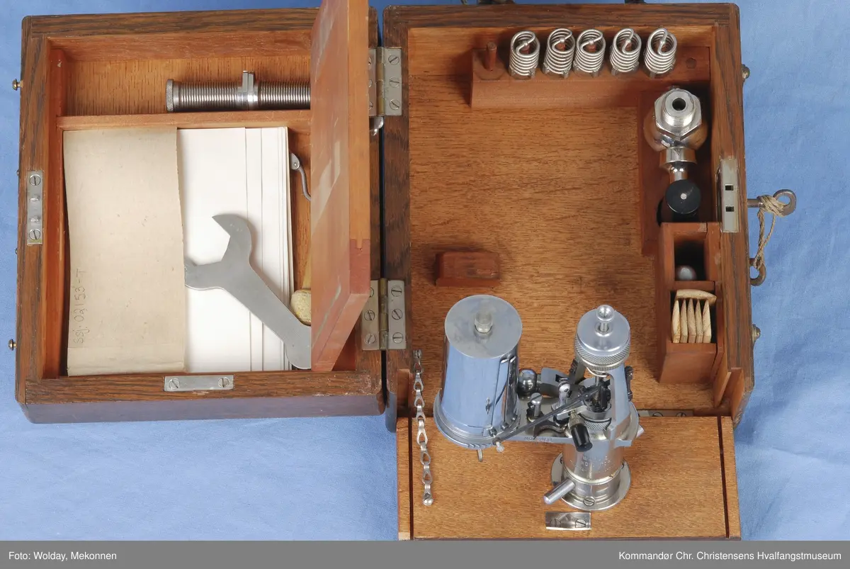 Indikatoren ligger i en trekasse m. diverse tilbehør. Indikatoren ble brukt til å måle trykket dvs. effekten av maskinen. Instrumentet tegnet diagram som kunne leses av for å beregne virkningsgrad, trykk, lekkasjer o.l