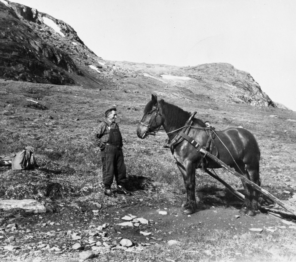 Martin Nilsen fra Vassdalen med hest. Ryggsekk på en stein. Nilsen f. 1903 var kjørekar i Sverige i mange år. Bildet er tatt der.