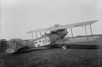 Flygplan FVM S 18 märkt nummer 996 med flygförare och flygspanare på ett flygfält på Flygkompaniet på Malmen. Militärer står omkring flygplanet. Fotograferat snett bakifrån.