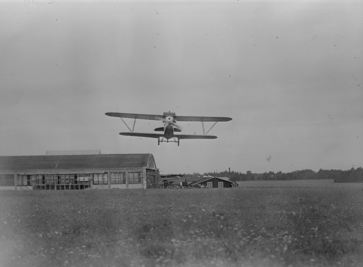 Flygplan Phönix E 2 Dront landar på flygfält. Flyghangar i bakgrunden.