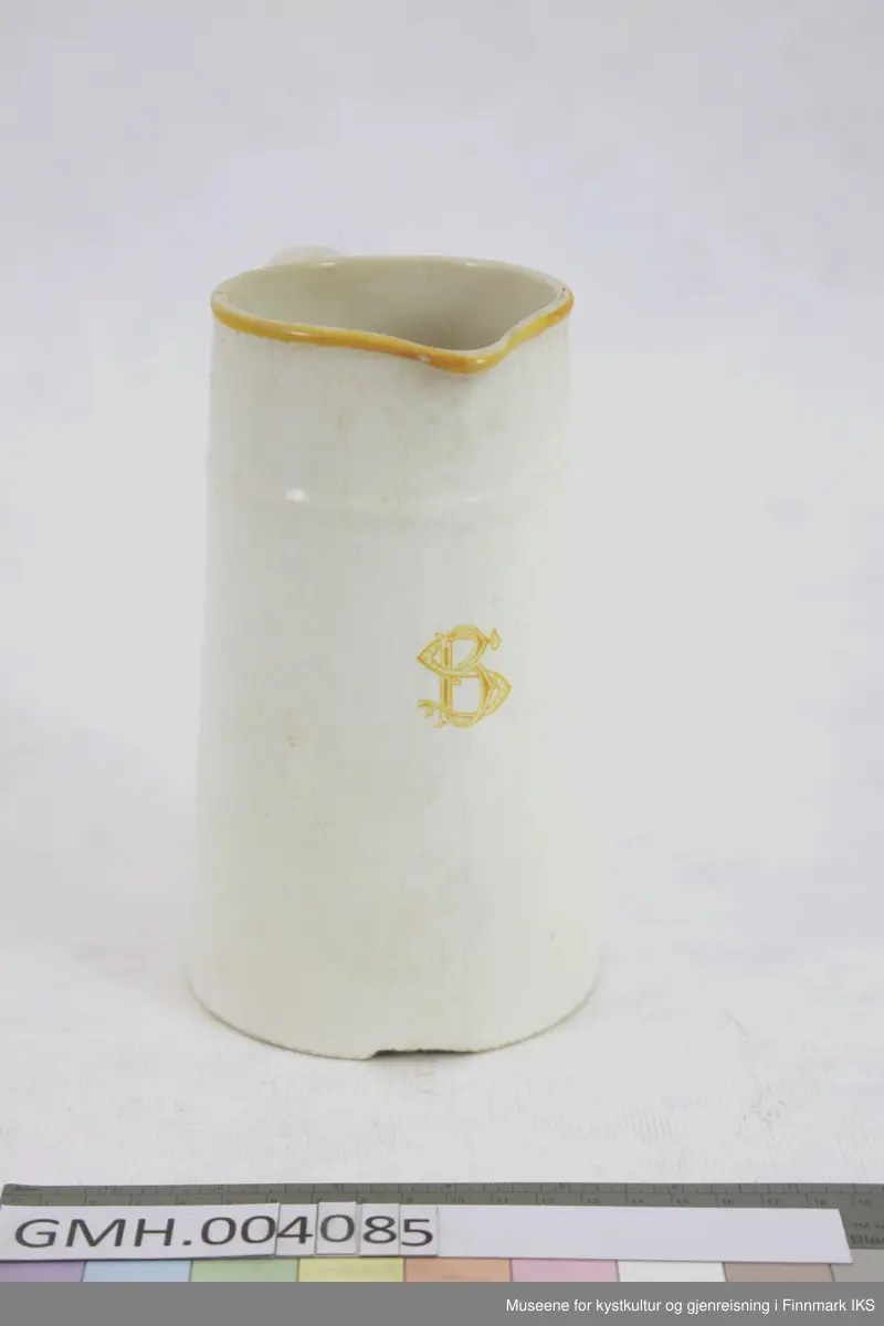 Muggen er utført i porselen med gule detaljer. Framsiden av muggen er dekorert med de ornamenterte bokstavene SB og en malt dekorasjonskant øverst. Muggen har en konisk form og på øvre del finnes en horisontal stav som dekorativt element. Håndtaket, som også har en malt dekorasjon, har en dyptgående sprekk i nedre del.