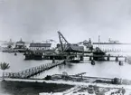 Fotografi från Karlskrona förmodlingen 1898.

I bakgrunden under mastkranen ligger den avrustade ångkorvetten SAGA.