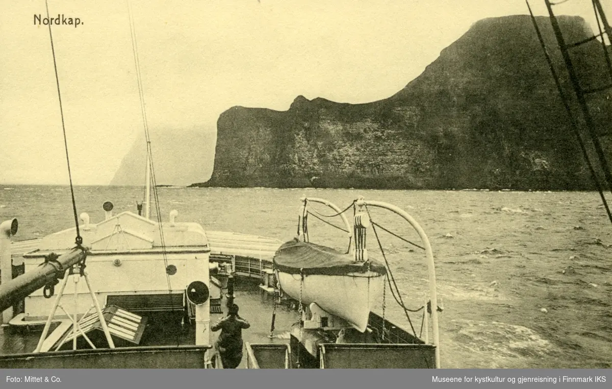 Postkort. Fordekket av turistbåt. Nordkapp i bakgrunnen(?). Usikkert om motivet virkelig viser Nordkapp. Fjellet til høyre er f.eks. for høy.