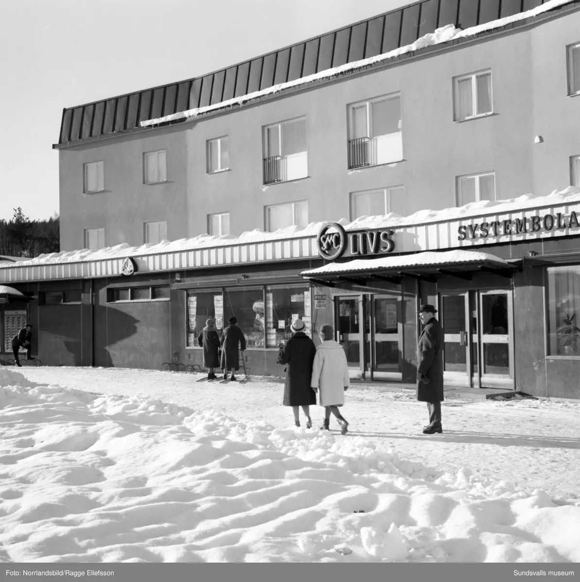 Hus, gator och människor i Timrå. Området Tallbacken med bronsskulpturen Smålandsflickorna av Thorwald Alef, Mariedalsskolan, en korvkiosk vid Köpmangatan och simhallen.