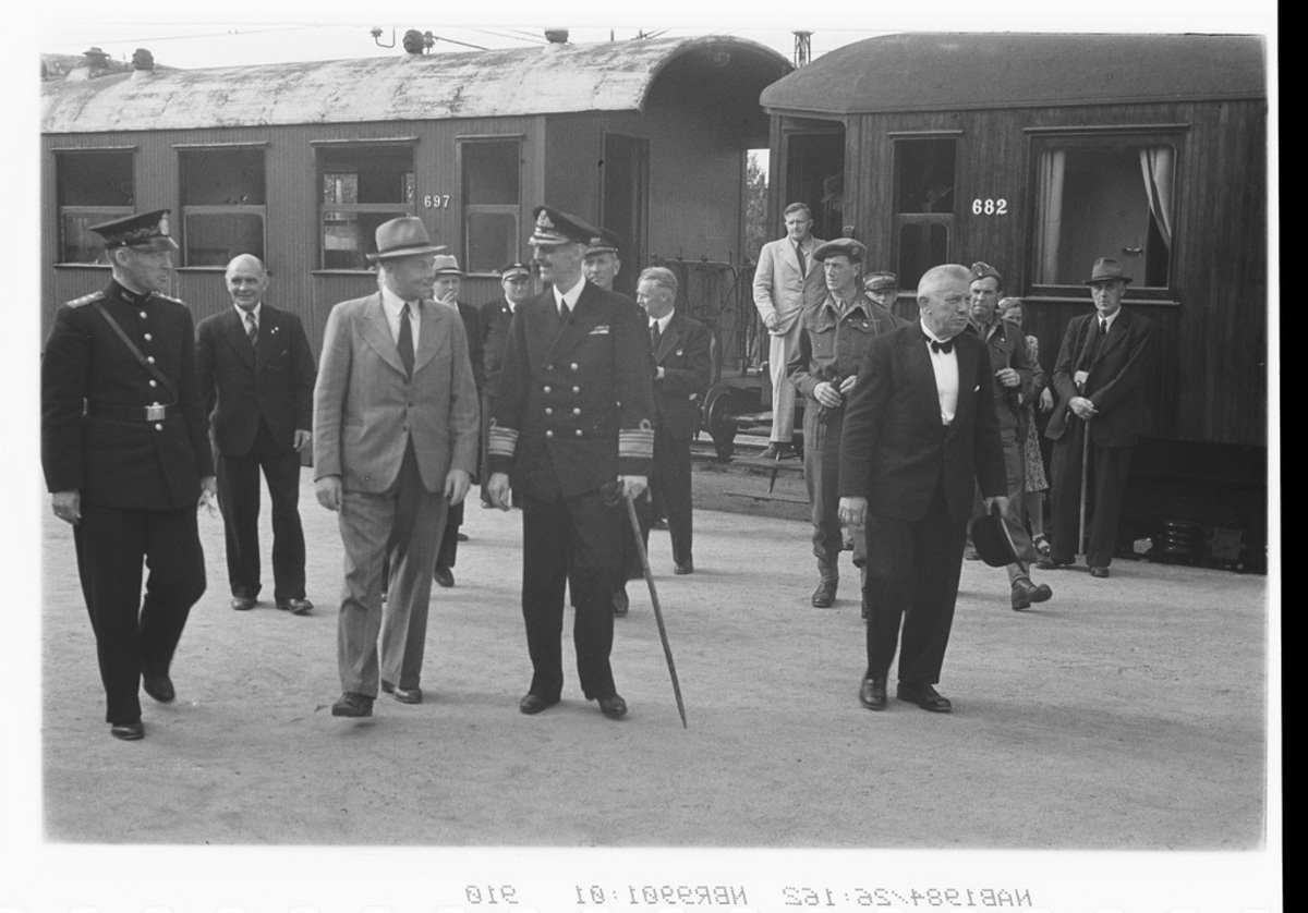 Ettter lunch på Royal gikk det tog til Bjørnfjell med kong Haakon og innbudte.  Foto på  Narvik stasjon.  Tra venstre: Politimester ?. inspektør Trætteberg, NSB (formann i festkommiteen for den etterfølgende kongemidagen på Royal), , ordfører Alfred Nilsen. På stigtrinnet står slakter Lindqvist ?   Jac. Kuvaas  forran med hatten i hånd.
Jernbanevognene er Bo 697 og ABo 682 "Kongevogna".