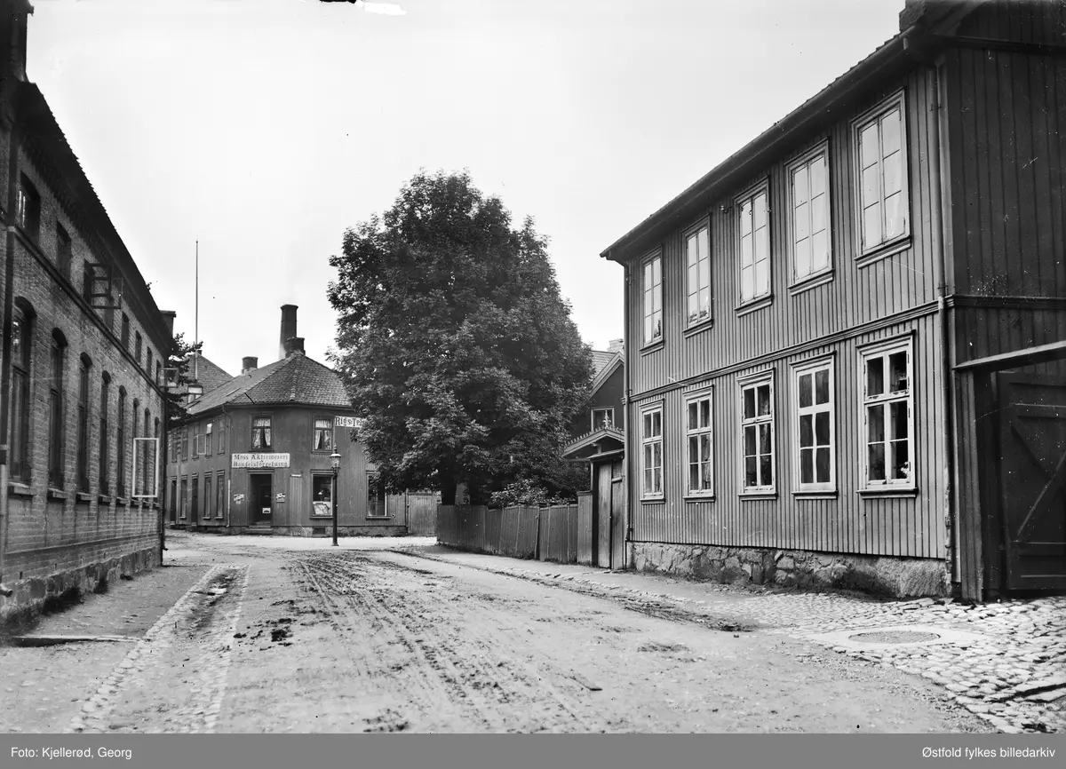 Gateparti fra Moss 1910, Fleischers gate. Moss Aktiemerieri og Handelsforretning i enden av gata, adresse Fleischersgate 7. På veggen reklameskilt for Rigstelegraf.

Den kryssende gata er Værlegata som går ned til høyre.
Før reguleringen og byggingen av Rådhusbrua fra Kanalen og opp på Thornløkka gikk Fleischersgate fra Storgaten og opp til krysset Høienhaldgt/Vogtsgate. Værlegaten gikk fram til Fleishersgt. og fortsatte over i Kirkegaten. Dette gatesystemet ble brutt ca. 1974 da man bygget nytt Rådhus,samfunnshus og Bank her (arkitektkonkurransen vunnet av mossearkitektene; Nærby, Jansen og Ording). (Info fra: Hermod Ludvigsen 2015).


Moss byleksikon: 
Moss Aktiemeieri lå i Fleischers gate 7, ble stiftet i 1899 etter mange års planlegging. I en del av første etasje ble det etablert en handelsforretning, og meieri i resten av huset. I bakgården var det stall for syv meierihester. 

2.juli 1900 ble den første melken tatt i mot fra bønder i Moss og Jeløy. En del av melken ble brukt til å lage ost, smør og fløte. Melken ble kjølt ned av is, først i 1915 ble det kjøpt et kjøleanlegg. I september åpnet melkeutsalget i egen butikk i den gamle hjørnegården. De første årene gikk meieriet mer eller mindre med tap. Et forsøk på å øke prisene førte til at 150 husmødre i Moss nektet å kjøpe melk på meieriet. Men de kom ingen vei. I 1913 var omsetningen så stor at meieriet måtte kjøpe naboeiendommene for å bygge ut. 

Fra 1920 begynte bøndene i Rygge å levere melk til Moss i stedet for til Dilling meieri og Værne Kloster meieri som sluttet med melkemottak. 

I 1944 gikk Aktiemeieriet over til andelsselskap. Etter hvert ble det også flere melkeutsalg rundt om i byen. Flaskemelk ble innført i 1949. Moss Aktiemeieri ble nedlagt i 1973. Meieriutsalget i Fleischers gate ble nedlagt i 1981, og like etter ble deler av meieribygningen revet.