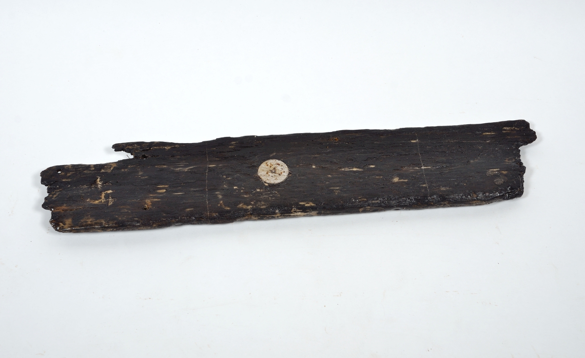 Möjligen en del av ett bord till en mindre båt. Den ena änden är avbruten, den andra utgörs av en bladlask med lång avfasning. Bevarad längd på fasningen är 130 mm men kan ha varit något längre ty kanten är avbruten. Bladlaskens fasning är  avgränsad av en tydlig ristad linje som bör har visat båtbyggaren var lasken skall börja. Den ena långsidan kan vara nära sin ursprungliga fason. Här finns en svag skålad ränna som kan vara en drevränna. I denna sitter ett bevarat spikhål. Ytterligare tre spikhål finns i bladlasken. Spikhålen är fyrkantiga. Den andra långsidan kan vara avbruten. Detta är svårt att säga säkert då ytan till största delen är anfrätt. Verktygsspår, sannolikt efter yxa, syns på laskens rätt så välbevarade yta.