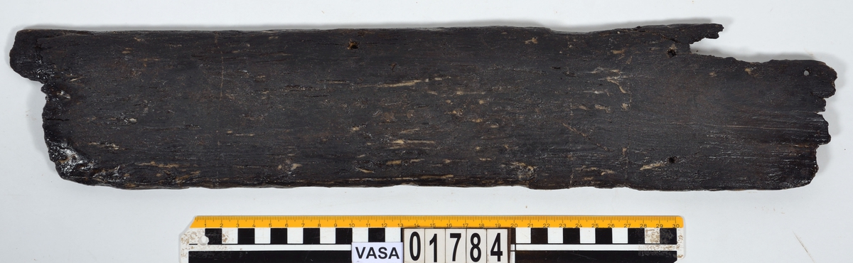 Möjligen en del av ett bord till en mindre båt. Den ena änden är avbruten, den andra utgörs av en bladlask med lång avfasning. Bevarad längd på fasningen är 130 mm men kan ha varit något längre ty kanten är avbruten. Bladlaskens fasning är  avgränsad av en tydlig ristad linje som bör har visat båtbyggaren var lasken skall börja. Den ena långsidan kan vara nära sin ursprungliga fason. Här finns en svag skålad ränna som kan vara en drevränna. I denna sitter ett bevarat spikhål. Ytterligare tre spikhål finns i bladlasken. Spikhålen är fyrkantiga. Den andra långsidan kan vara avbruten. Detta är svårt att säga säkert då ytan till största delen är anfrätt. Verktygsspår, sannolikt efter yxa, syns på laskens rätt så välbevarade yta.