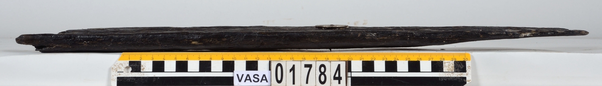 Möjligen en del av ett bord till en mindre båt. Den ena änden är avbruten, den andra utgörs av en bladlask med lång avfasning. Bevarad längd på fasningen är 130 mm men kan ha varit något längre ty kanten är avbruten. Bladlaskens fasning är  avgränsad av en tydlig ristad linje som bör har visat båtbyggaren var lasken skall börja. Den ena långsidan kan vara nära sin ursprungliga fason. Här finns en svag skålad ränna som kan vara en drevränna. I denna sitter ett bevarat spikhål. Ytterligare tre spikhål finns i bladlasken. Spikhålen är fyrkantiga. Den andra långsidan kan vara avbruten. Detta är svårt att säga säkert då ytan till största delen är anfrätt. Verktygsspår, sannolikt efter yxa, syns på laskens rätt så välbevarade yta.
