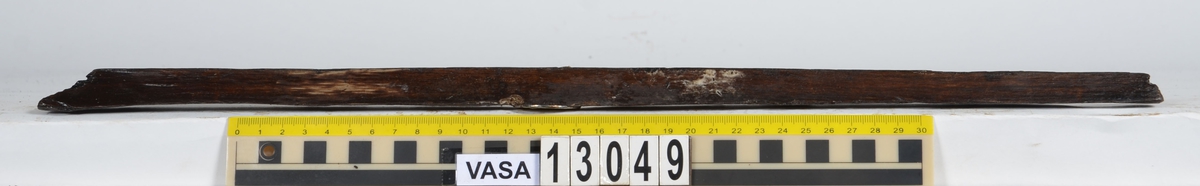 Splitter.  Svagt kilformat tvärsnitt. Båda ändarna avbrutna Ena långsidan är bortspjälkad, den andra är fasad. En av ytorna visar spår efter att ha blivit bearbetad av yxa eller (troligare) skavjärn. Den andra sidans yta uppvisar karaktäristiska spår efter skavjärn.

Möjligen är detta en del av en laggstav till en tunna. Dimensionerna, de stående årsringarna samt fyndkontexten talar för detta.
