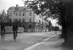 Bostadshus kantar Brunnsgatan i Jönköping där två män cyklar. Längst bort, österut, skymtar tornen på Helmershus, numera rivet.