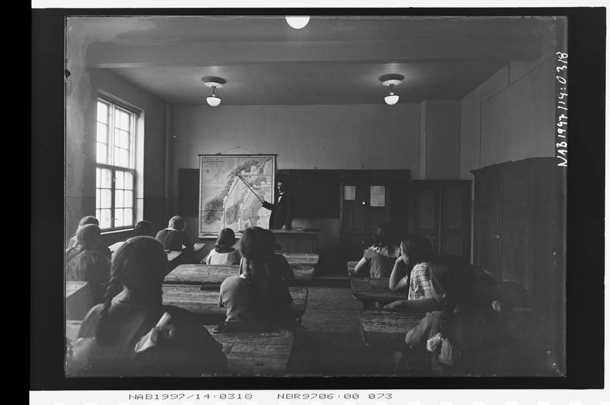 Fra gamle middelskolen (Grønnskolen)- klasserom.
Ved katteret, rektor Rødseth som peker på Narvik på norgeskartet. Skolelpulter.