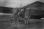 Grupporträtt. En flygmekaniker och en flygförare framför flygplan Thulin A /Bleriot XI på Flygkompaniet på Malmen, 1915. I bakgrunden syns en hangar.