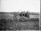 Porträtt av tre herrar med bil. Hunne el. Halleberg i bakgrunden.